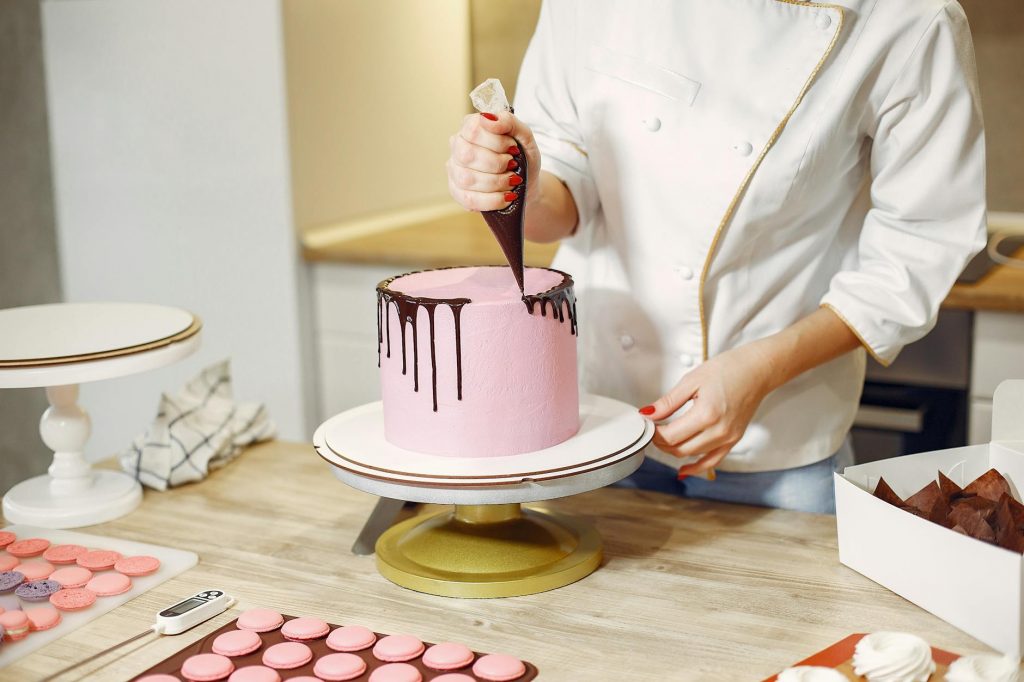 Female pastry cook decorating cake with chocolate in kitchen