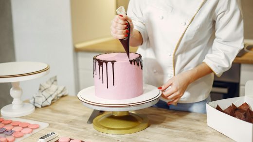 Female pastry cook decorating cake with chocolate in kitchen