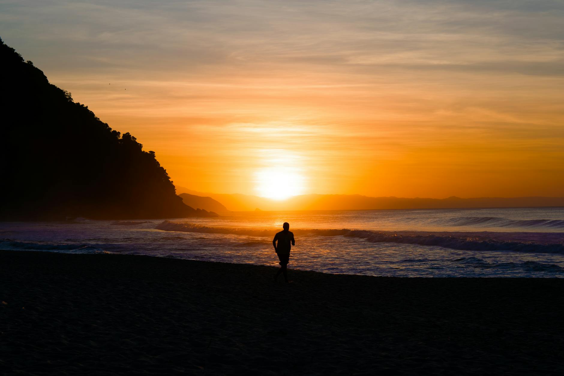 silhouette of person jogging along a sunset beach
