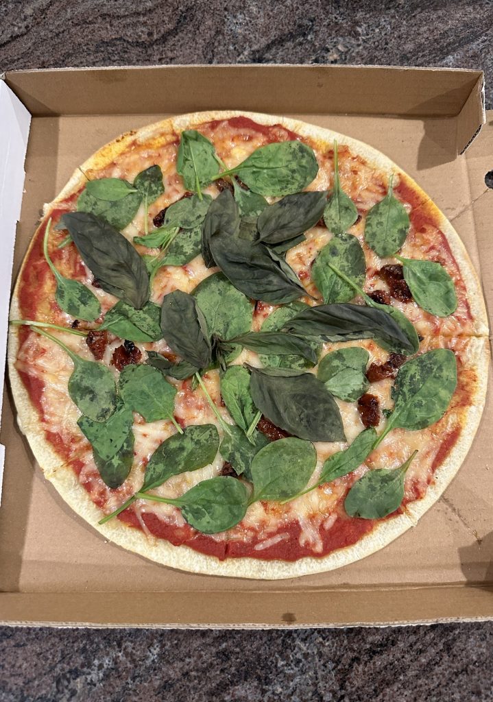 Gluten-free pizza with green leaves from Amora Pizza in Doha, Qatar.